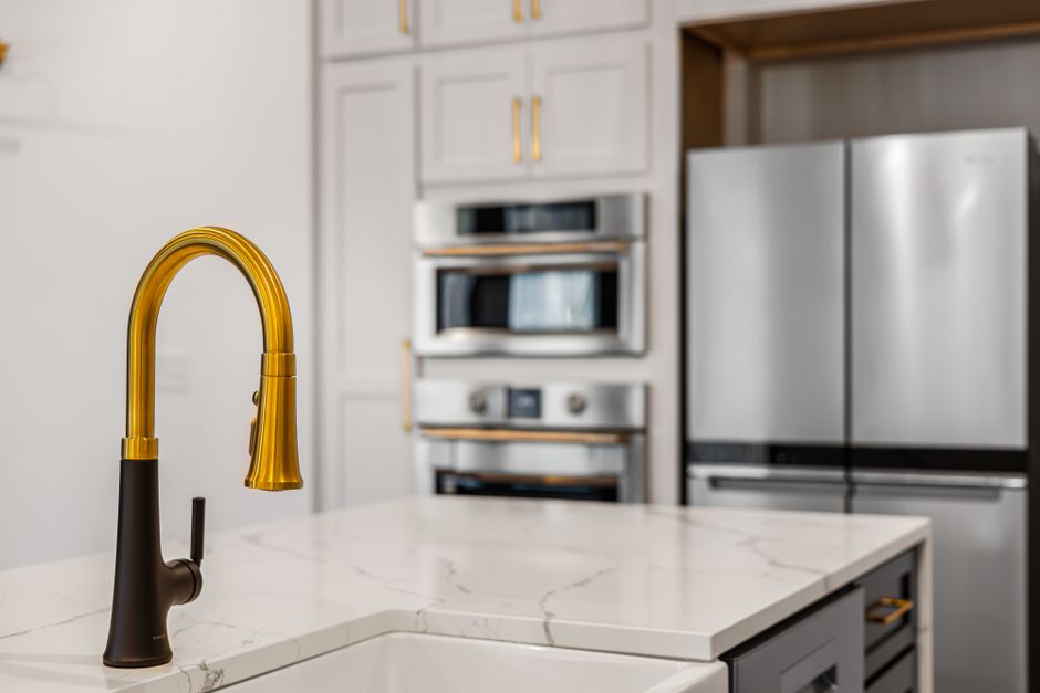 Elegant kitchen interior with a modern gold faucet and sleek stainless steel appliances.